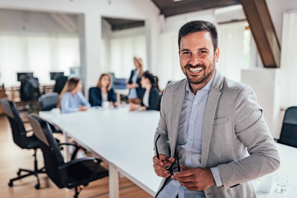 Professional business man sitting on a conference room table with three other employees behind him