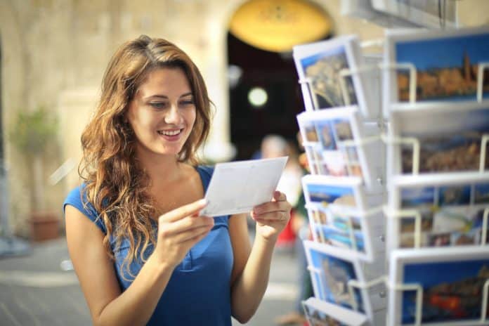 Woman holding a postcard in front of a stand filled with postcards