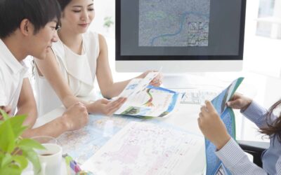 A couple reviewing a printed brochure, while the person on the other side of the desk folds another pamphlet.