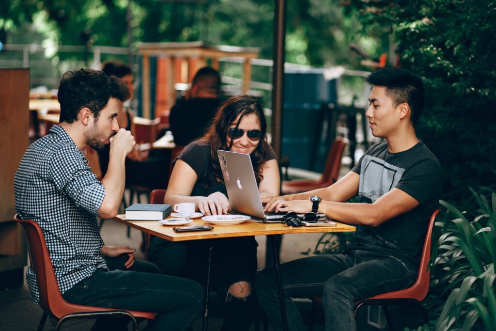 Three people sitting at a table around a laptop smiling and working