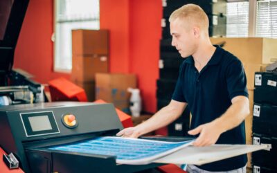 Young man working in printing factory. Man is grabbing prints from the digital printing press