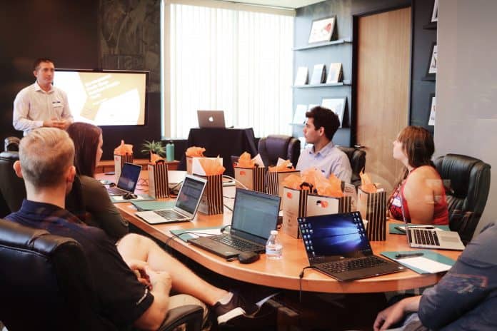 Employees sitting around a conference table with someone presenting in front of a tv