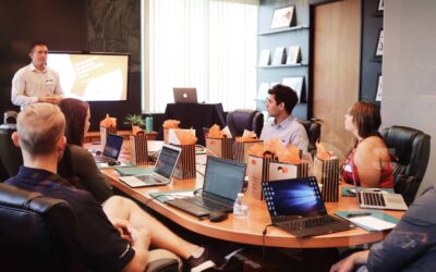 Employees sitting around a conference table with someone presenting in front of a tv