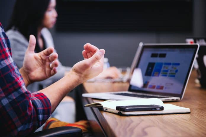 Close up on a person gesturing with their hands infront of a laptop on a conference table.