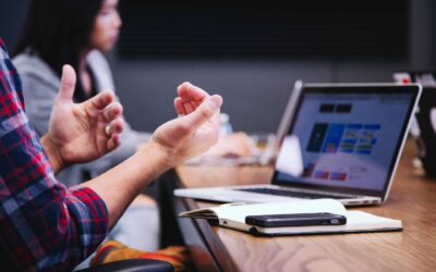 Close up on a person gesturing with their hands infront of a laptop on a conference table.