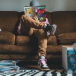 Young man sitting on sofa and reading comics magazine